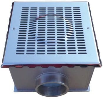 Square stainless-steel floor drain with slotted grate sits facing upward, channeling water through a protruding circular side outlet in a plain studio setting.